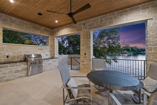 patio terrace at dusk with an outdoor kitchen, a water view, and ceiling fan