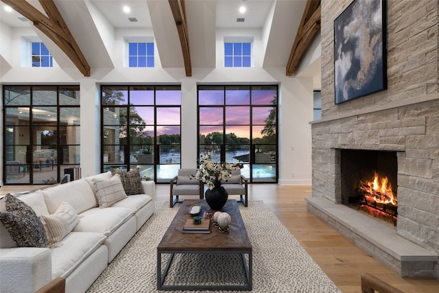 living room featuring beam ceiling, a fireplace, a high ceiling, and light wood-type flooring