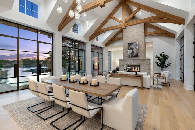 dining room featuring high vaulted ceiling, a water view, a fireplace, beamed ceiling, and light hardwood / wood-style floors