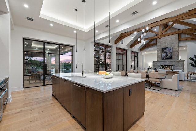 kitchen with sink, a stone fireplace, light hardwood / wood-style flooring, a large island with sink, and dark brown cabinets