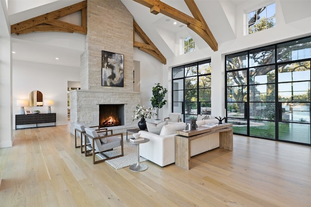 living room with beam ceiling, a stone fireplace, high vaulted ceiling, and light wood-type flooring