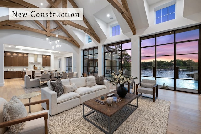 living room with beamed ceiling, high vaulted ceiling, a chandelier, a water view, and light wood-type flooring