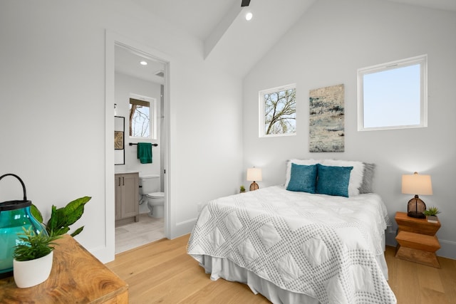 bedroom with multiple windows, vaulted ceiling, ensuite bathroom, and light wood-type flooring