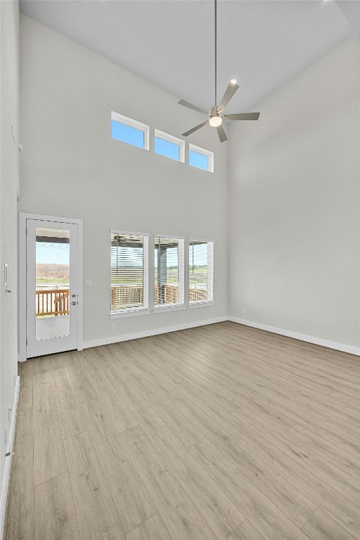 unfurnished living room featuring a towering ceiling, light hardwood / wood-style flooring, and ceiling fan