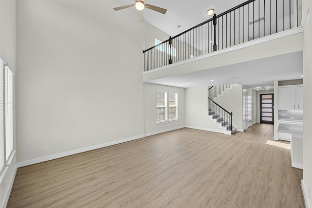 unfurnished living room with ceiling fan, light wood-type flooring, and a towering ceiling
