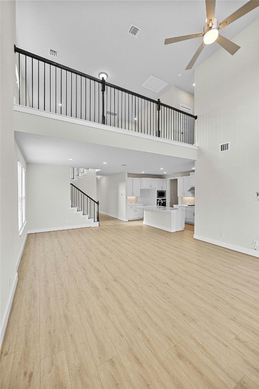 unfurnished living room featuring a towering ceiling, light hardwood / wood-style floors, and ceiling fan