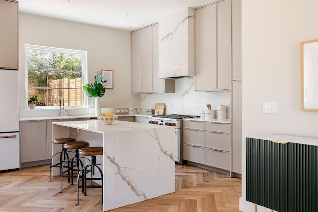 kitchen featuring a breakfast bar, high end stove, light parquet floors, sink, and white refrigerator