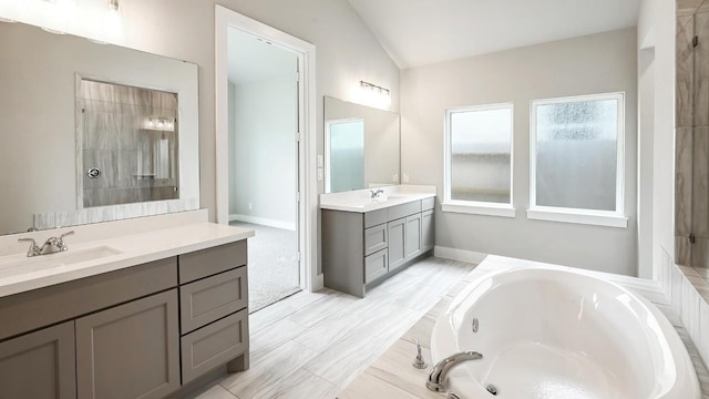 bathroom with vanity, tiled bath, and vaulted ceiling