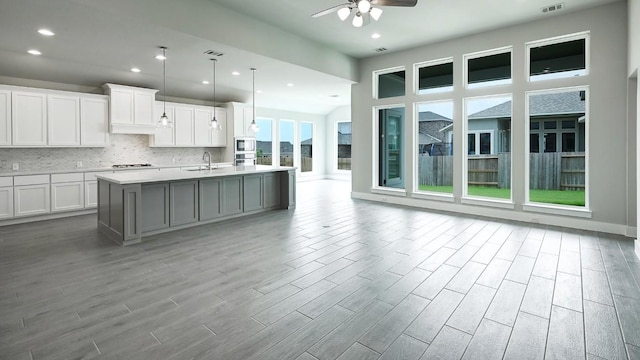 kitchen featuring a center island with sink, decorative light fixtures, light hardwood / wood-style floors, and white cabinetry