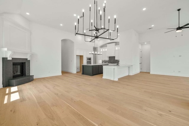 unfurnished living room with a fireplace, ceiling fan with notable chandelier, light hardwood / wood-style floors, and a towering ceiling