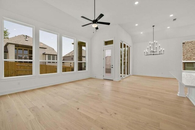 unfurnished living room with light hardwood / wood-style floors, a wealth of natural light, ceiling fan with notable chandelier, and vaulted ceiling