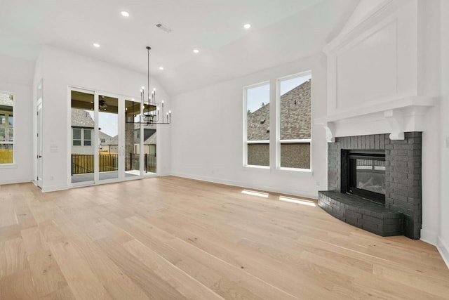 unfurnished living room with vaulted ceiling, a brick fireplace, light wood-type flooring, and a chandelier