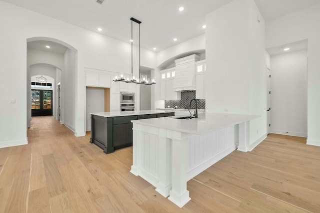 kitchen with white cabinetry, stainless steel appliances, pendant lighting, decorative backsplash, and light hardwood / wood-style flooring