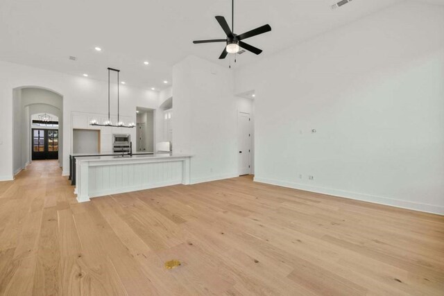 unfurnished living room featuring light wood-type flooring, ceiling fan, and a towering ceiling