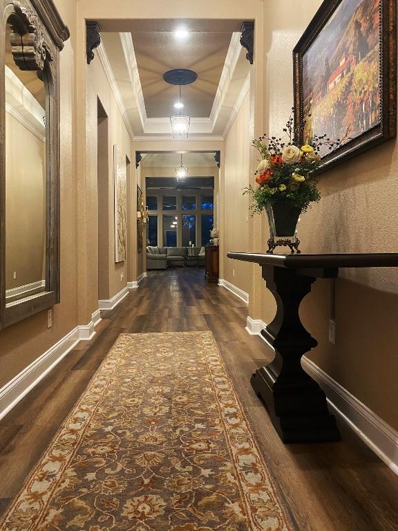 corridor with a raised ceiling, dark wood-style floors, baseboards, and crown molding