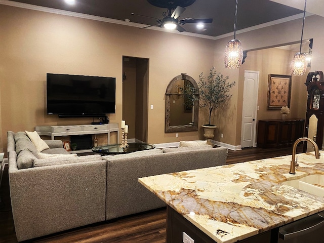 living area featuring a ceiling fan, baseboards, crown molding, and dark wood-type flooring