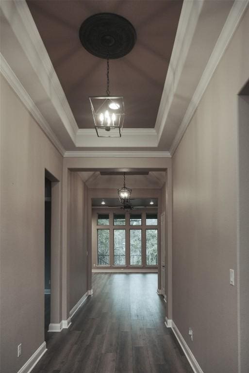 hall with dark wood-style floors, ornamental molding, a raised ceiling, and a notable chandelier