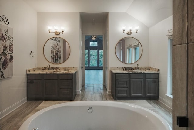 full bathroom featuring lofted ceiling, a tub, two vanities, and wood finished floors