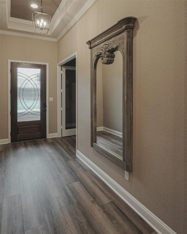 foyer entrance featuring a chandelier, baseboards, dark wood-style floors, a raised ceiling, and crown molding