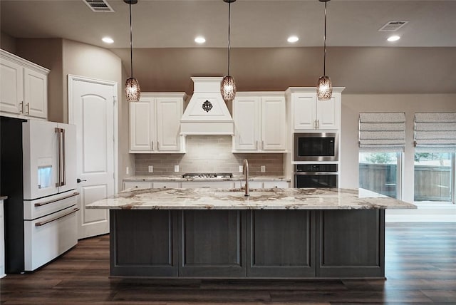 kitchen with stainless steel appliances, visible vents, white cabinets, a sink, and premium range hood