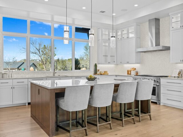 kitchen featuring sink, white cabinetry, a center island, stainless steel range, and wall chimney exhaust hood