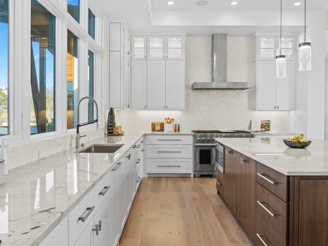 kitchen with sink, white cabinetry, high end range, light stone countertops, and wall chimney exhaust hood