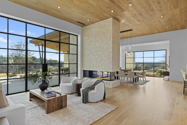 living room featuring a multi sided fireplace, a towering ceiling, wood ceiling, and light hardwood / wood-style floors