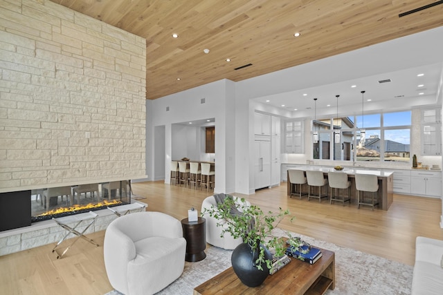 living room with a stone fireplace, wooden ceiling, and light wood-type flooring