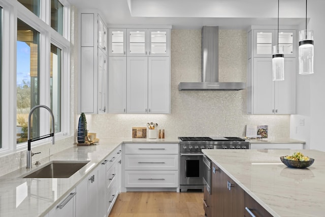 kitchen with white cabinets, stainless steel stove, light stone counters, and wall chimney exhaust hood