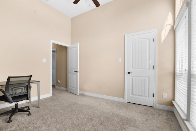 carpeted home office featuring ceiling fan and a towering ceiling