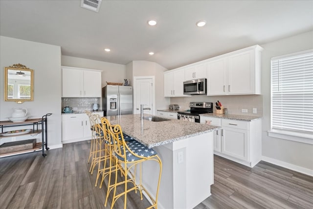 kitchen with backsplash, an island with sink, stainless steel appliances, hardwood / wood-style floors, and sink