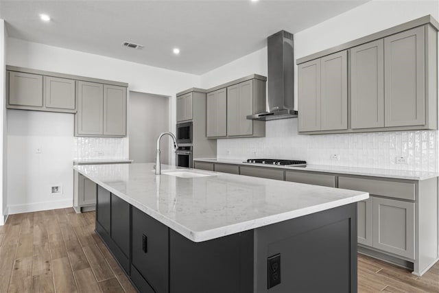 kitchen featuring wall chimney range hood, gray cabinetry, and a kitchen island with sink