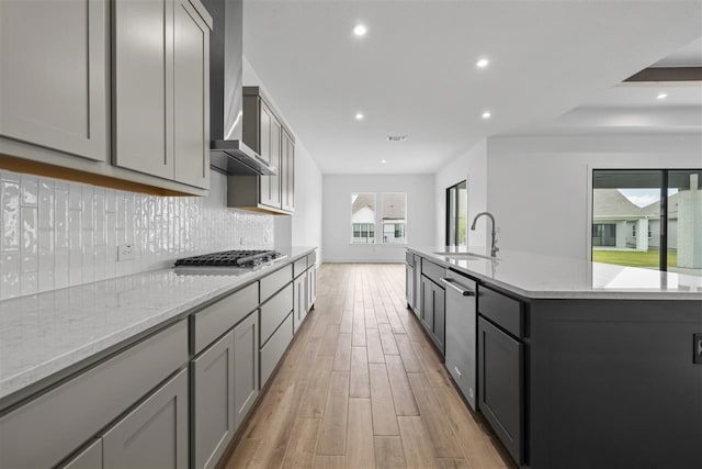 kitchen with stainless steel appliances, light hardwood / wood-style floors, wall chimney exhaust hood, sink, and gray cabinetry