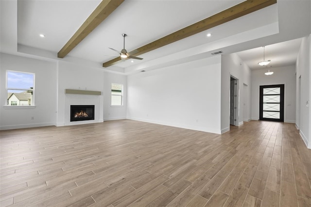 unfurnished living room featuring beamed ceiling, light wood-type flooring, and plenty of natural light