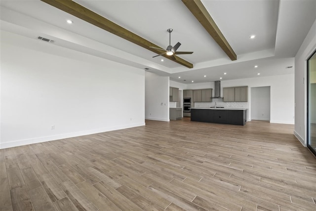 unfurnished living room with light hardwood / wood-style floors, ceiling fan, and beam ceiling