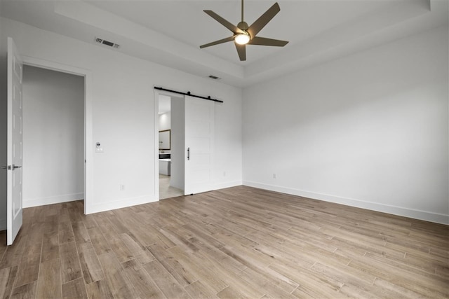 unfurnished bedroom featuring a barn door, light hardwood / wood-style floors, ceiling fan, and ensuite bath