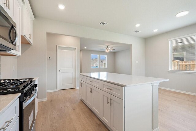 kitchen featuring light wood-type flooring, a kitchen island, ceiling fan, stainless steel appliances, and white cabinets