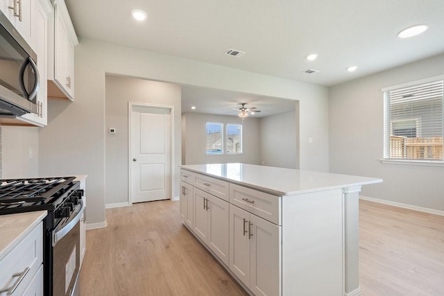 kitchen featuring ceiling fan, appliances with stainless steel finishes, white cabinetry, a center island, and light wood-type flooring