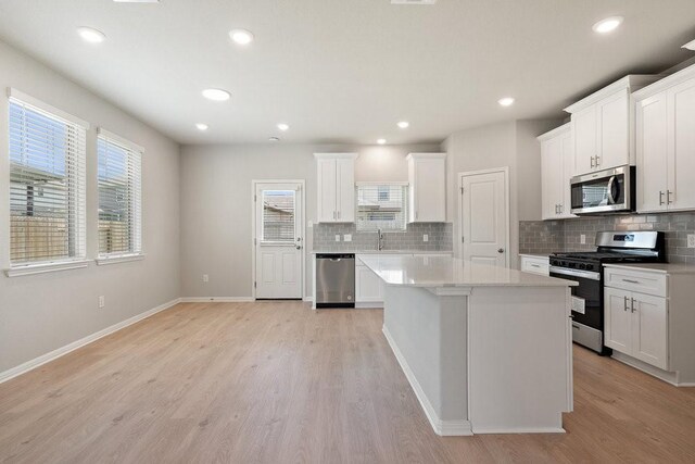 kitchen with white cabinetry, appliances with stainless steel finishes, a center island, and light wood-type flooring