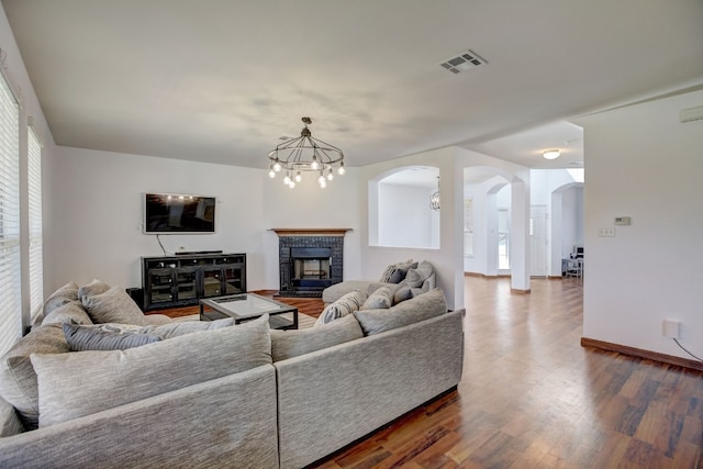 living area featuring arched walkways, a notable chandelier, a fireplace, dark wood-type flooring, and baseboards