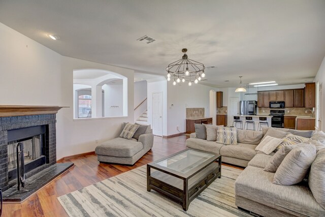 living room with sink, a brick fireplace, light wood-type flooring, and an inviting chandelier