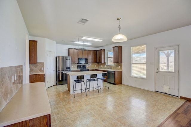 kitchen with visible vents, a kitchen island, black appliances, a kitchen bar, and backsplash