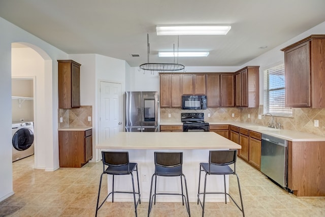 kitchen with a kitchen island, washer / clothes dryer, a breakfast bar, black appliances, and a sink