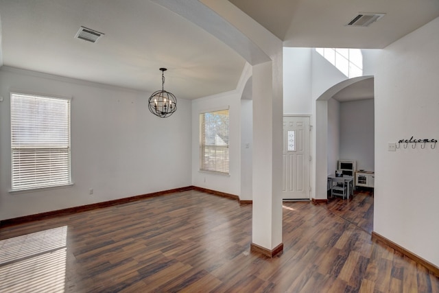 unfurnished room featuring arched walkways, dark wood-type flooring, visible vents, and baseboards