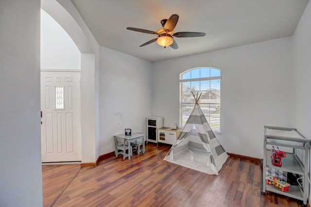 playroom featuring arched walkways, ceiling fan, wood finished floors, and baseboards