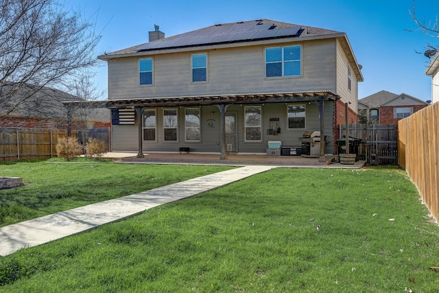 rear view of house featuring roof mounted solar panels, a fenced backyard, and a lawn