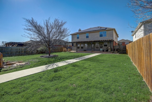 rear view of property with a yard, roof mounted solar panels, a fenced backyard, and a patio