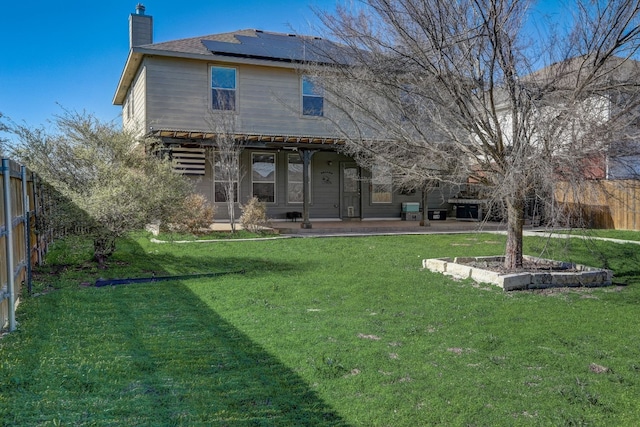 rear view of property featuring roof mounted solar panels, a fenced backyard, a lawn, and a chimney