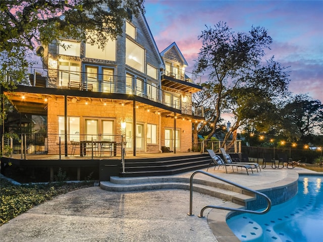 back house at dusk featuring a balcony, a fenced in pool, and a patio