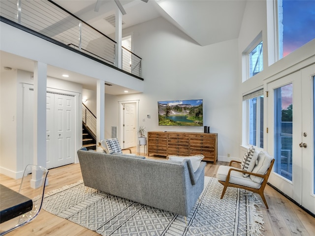 living room with french doors, light hardwood / wood-style floors, ceiling fan, and a towering ceiling